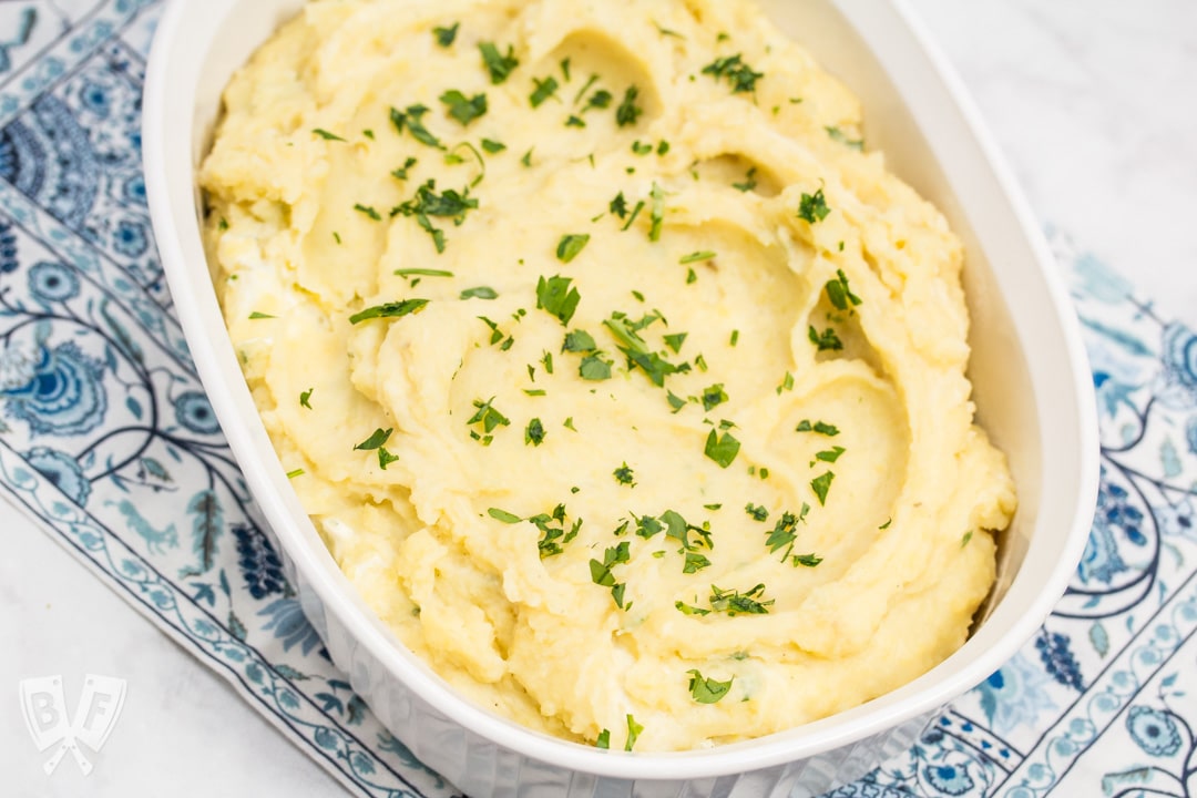 Overhead shot of an oval casserole dish full of creamy mashed potatoes sprinkled with chopped parsley.