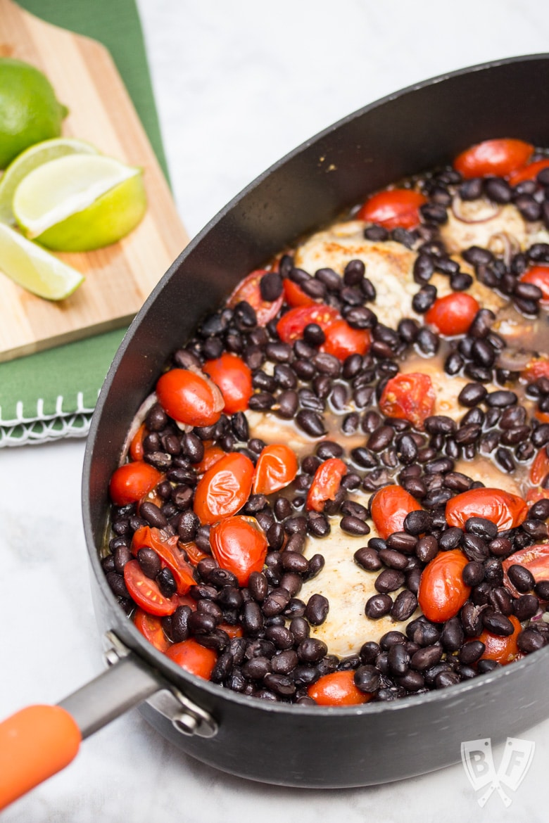 Overhead view up of a Latin Chicken Skillet with Black Beans + Tomatoes with a cutting board and limes off to the side.