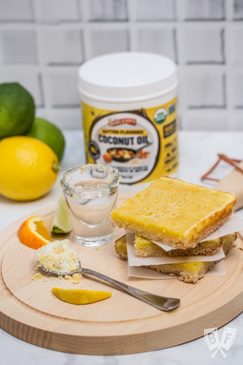 A stack of dessert bars with a shot of tequila, fresh citrus, and a jar of butter flavored coconut oil.