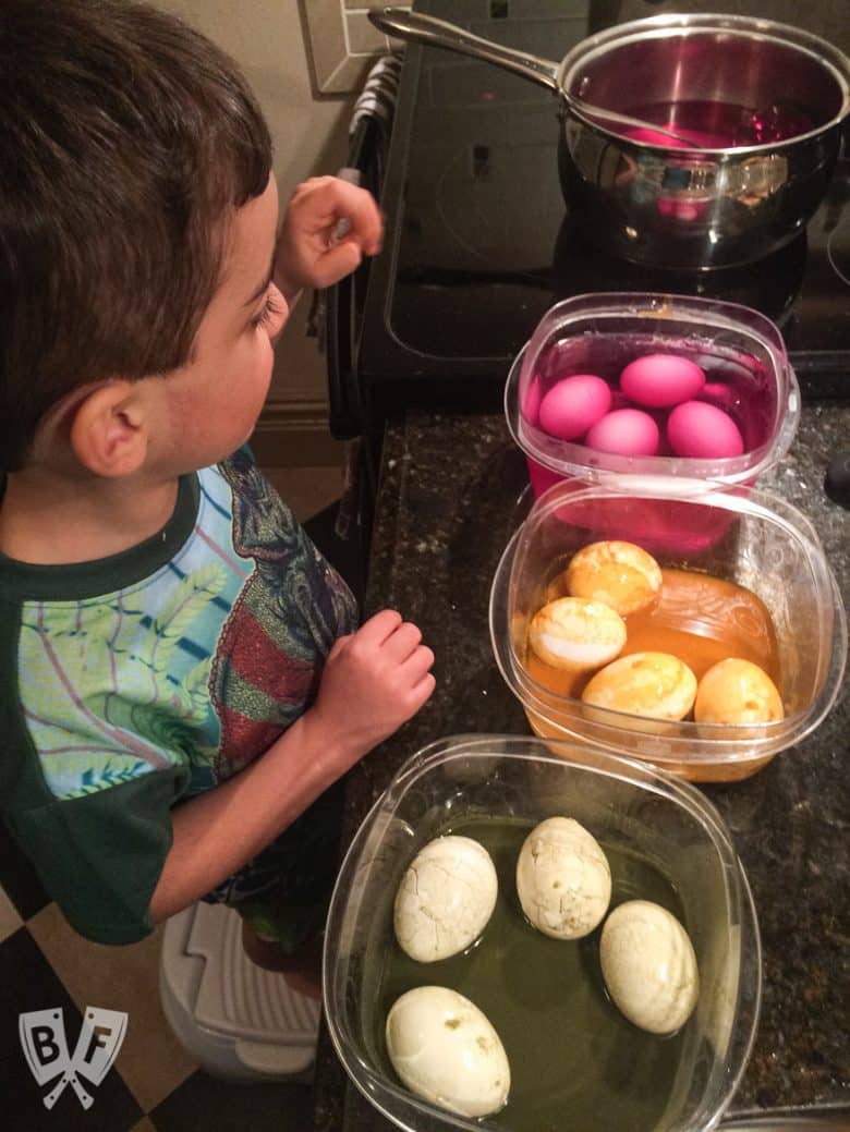 A child with bowls of Easter eggs soaking in natural egg dyes.