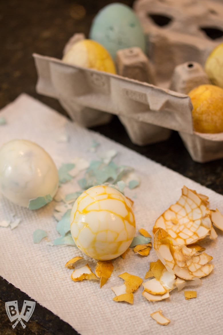 2 peeled, naturally dyed Easter egg with a cracked shell pattern and more Easter eggs in a carton in the background.