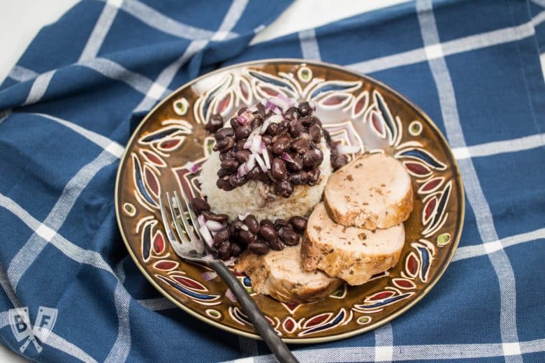 Overhead view of a plate of sliced pork tenderloin served with rice and beans