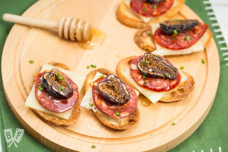 Honeyed Chorizo & Fig Crostini displayed on a board with a honey dipper.