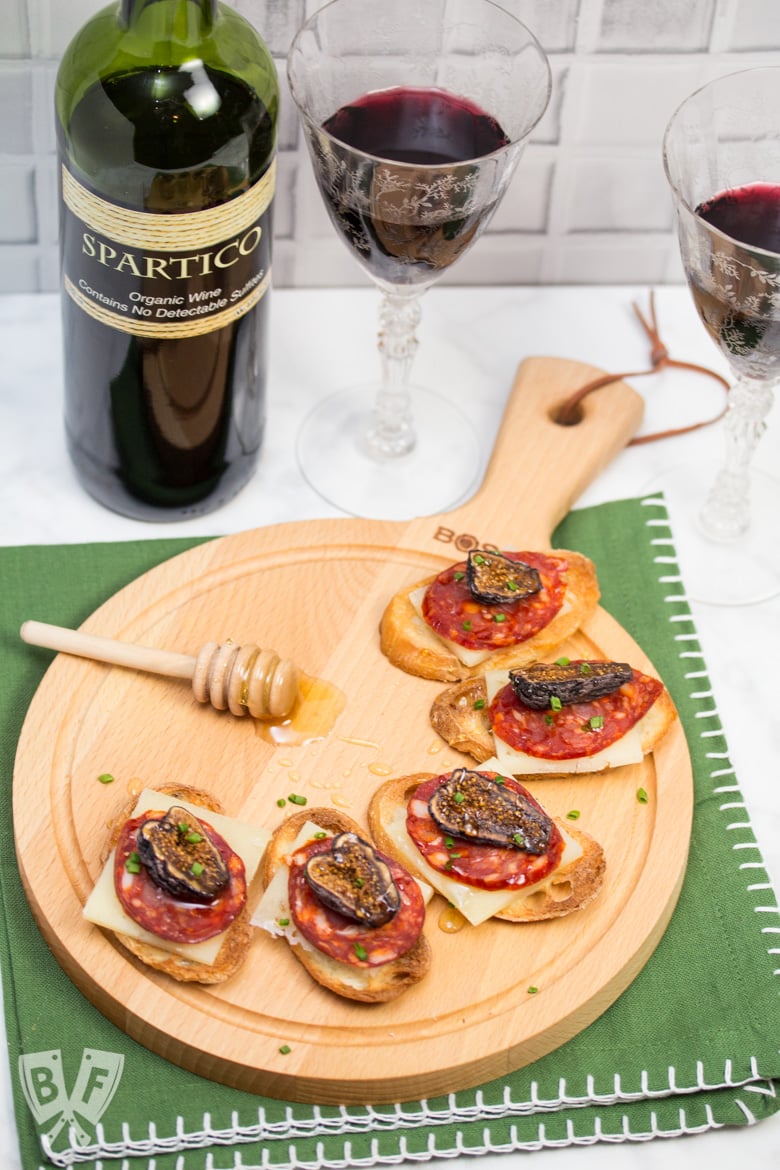 A board with honeyed chorizo and goat cheese crostini along with red wine.