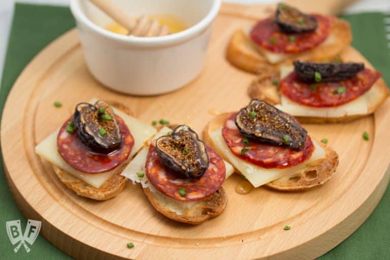 Crostini topped with manchego, chorizo, figs, and honey on a wooden board.