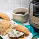 Side view of 3 assembled Instant Pot French Dip Sandwiches with au jus, and an Instant Pot alongside.