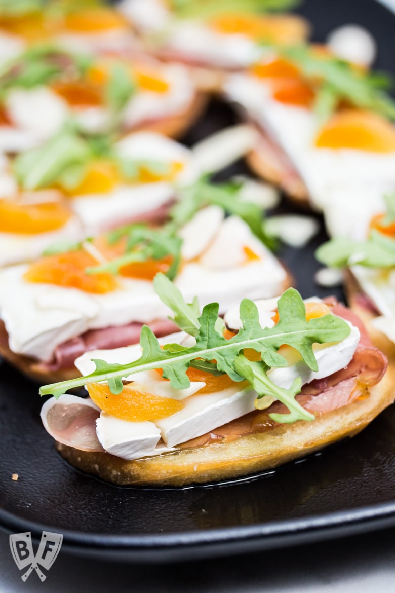 Close-up view of a platter of Prosciutto & Brie Crostini with Dried Apricots.