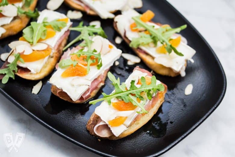 Close-up view of a platter of Prosciutto & Brie Crostini with Dried Apricots.