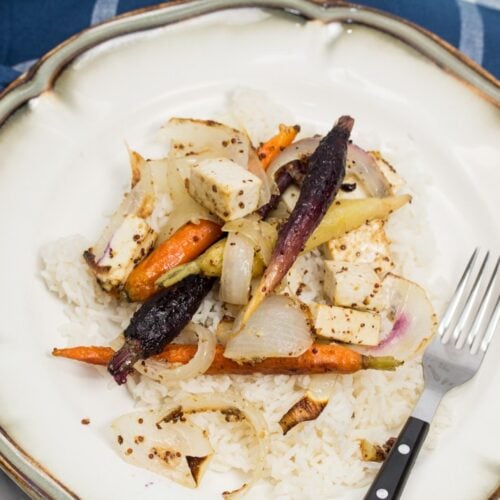 Overhead view of a plate of rice topped with roasted tofu, onions, and rainbow carrots.