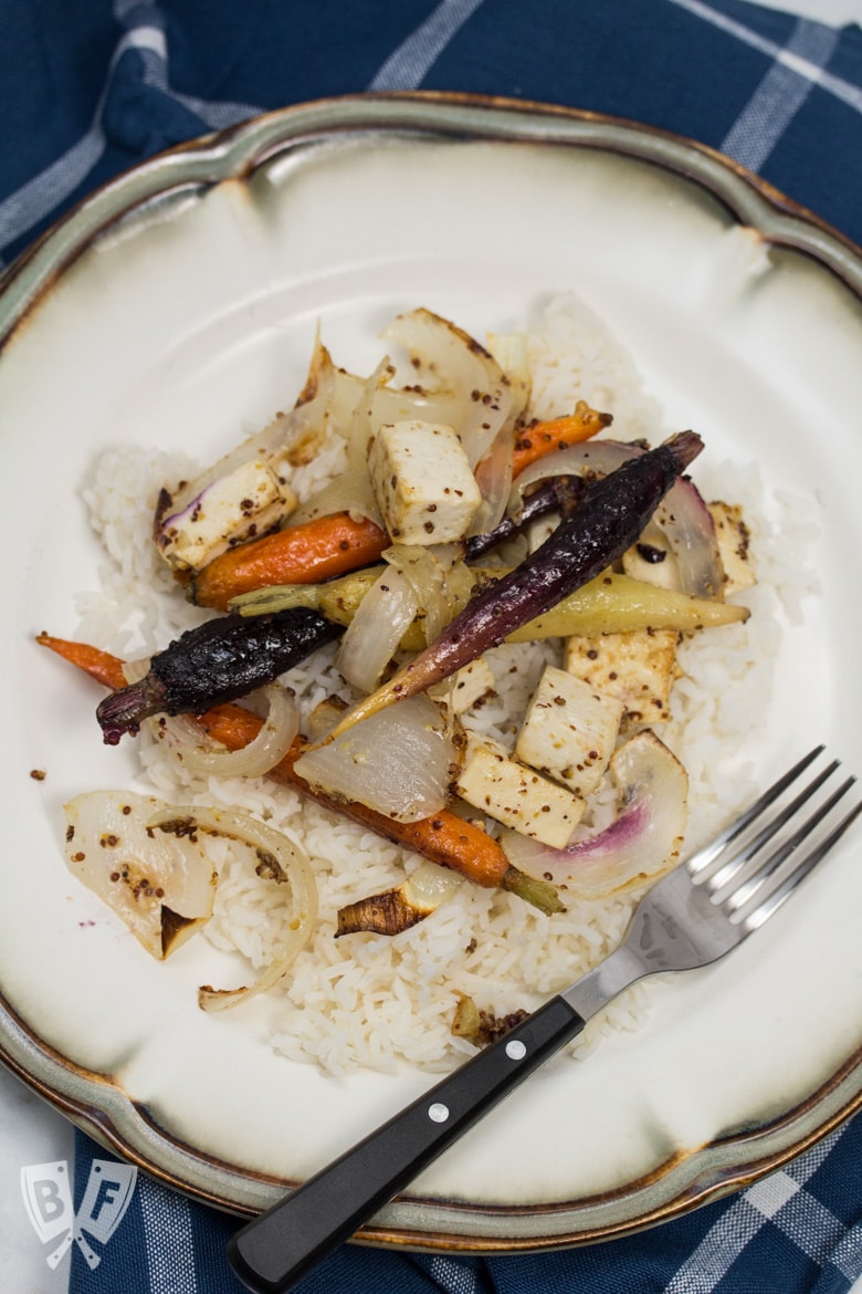 Overhead view of a plate of rice topped with roasted tofu, onions, and rainbow carrots.