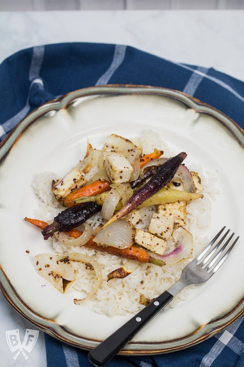 Overhead view of a plate of rice topped with roasted tofu, onions, and rainbow carrots.