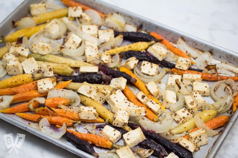 Overhead view of a sheet pan with roasted tofu, onions, and rainbow carrots.