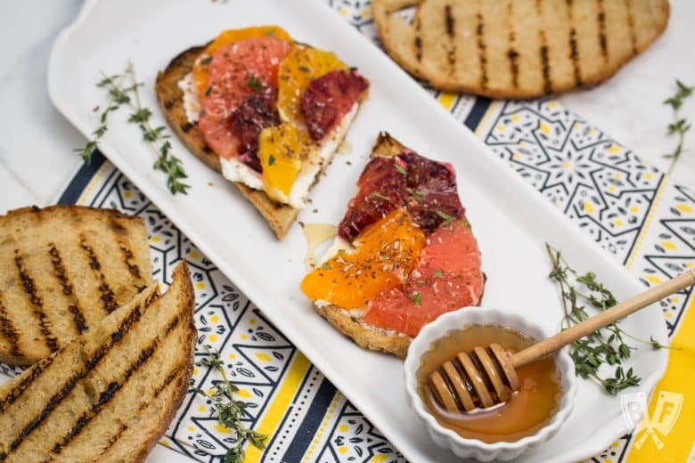 Overhead view of Goat Cheese Toast with Honeyed Citrus Fruit and ingredients around the sides.