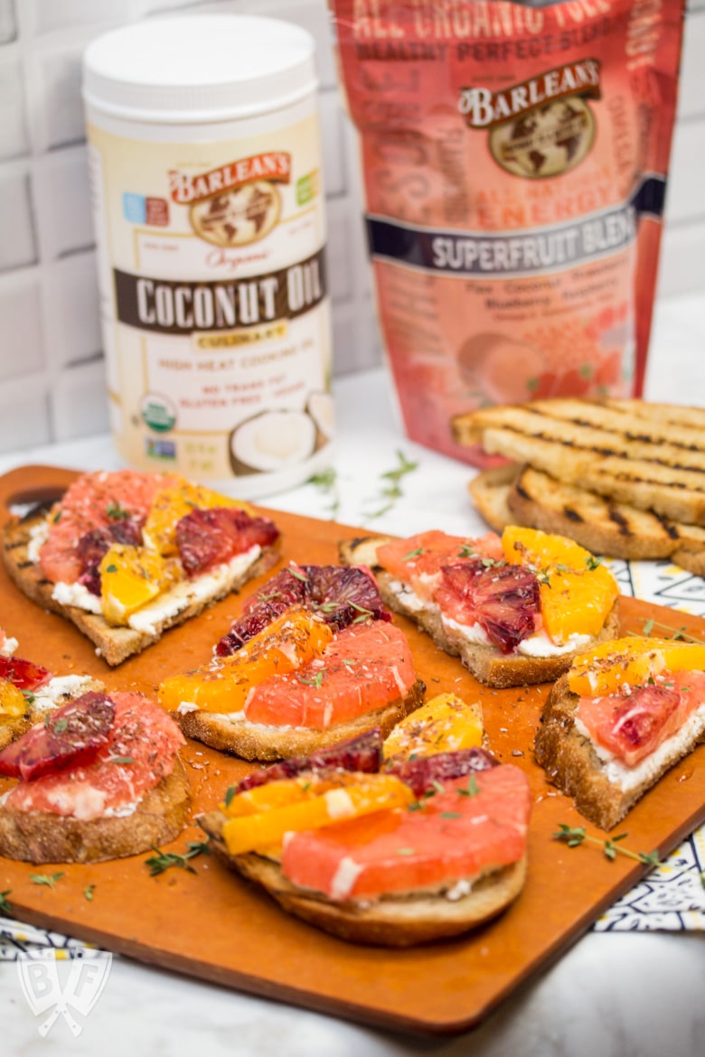 ¾ view of a board full of Goat Cheese Toast with Honeyed Citrus Fruit with ingredients around the sides.