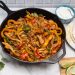 A cast iron skillet filled with chicken fajitas with tortillas and garnishes alongside.