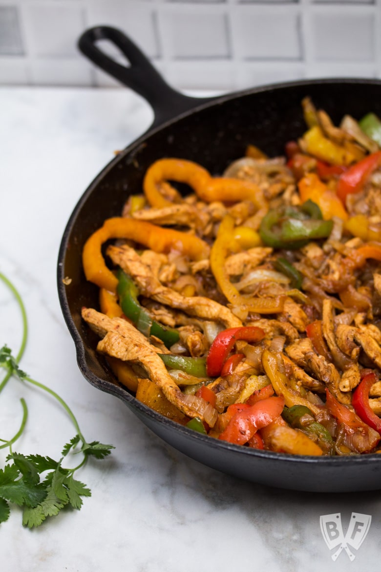 A cast iron skillet filled with chicken fajitas with tortillas and garnishes alongside.