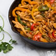 A cast iron skillet filled with chicken fajitas with tortillas and garnishes alongside.