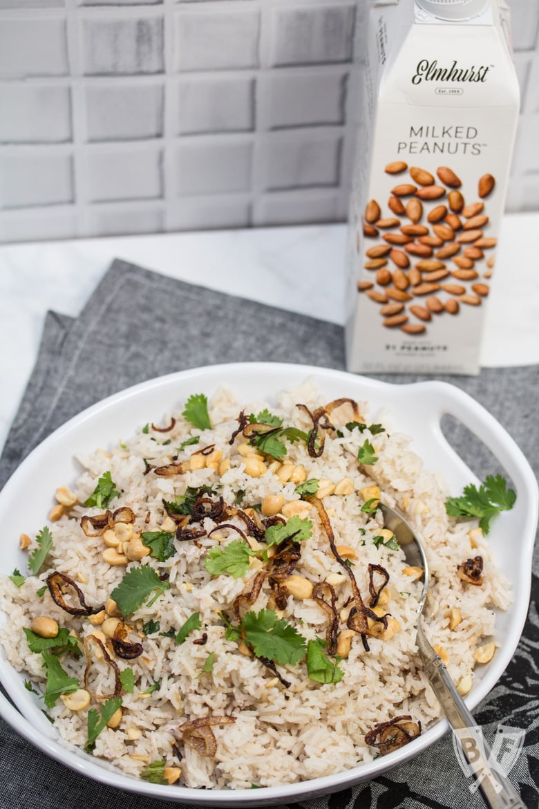 Overhead view of a bowl of Peanutty Rice with Crispy Fried Shallots and a carton of milked peanuts in the background.