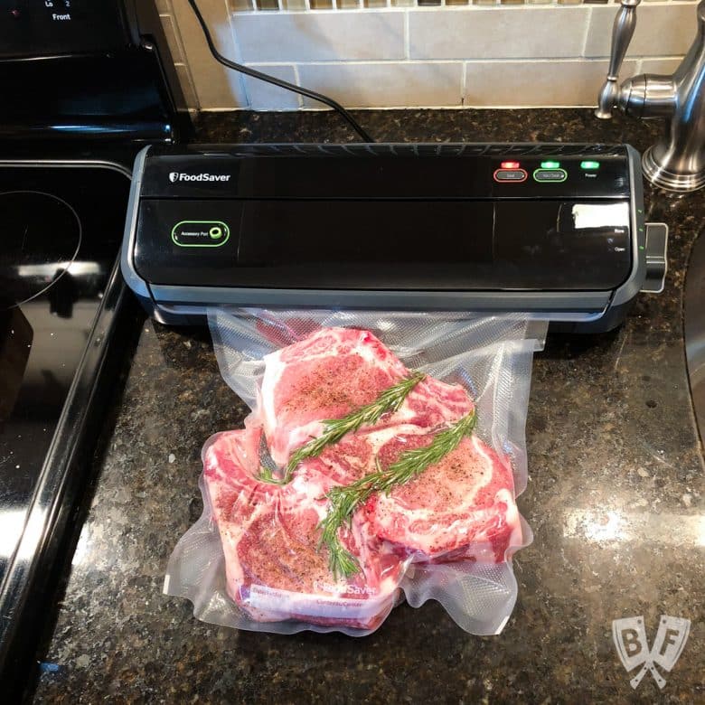 Overhead view of pork chops being vacuum sealed in a bag for sous vide cooking.