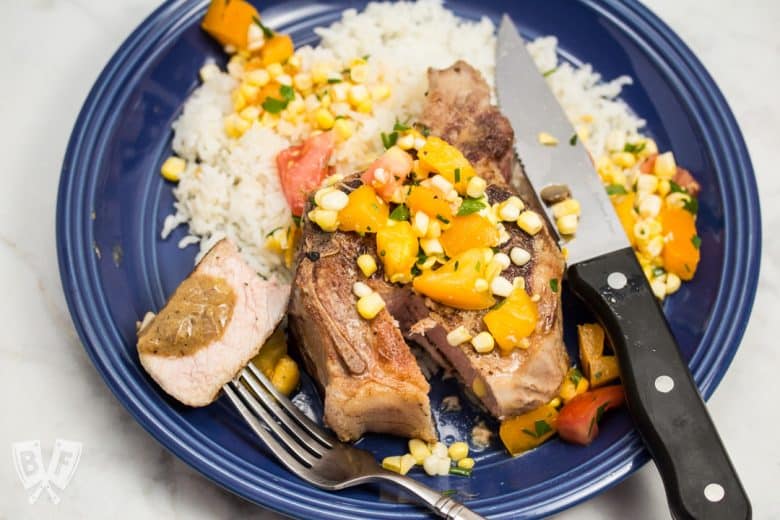 Overhead view of a pork chop over rice with a corn and tomato salad.