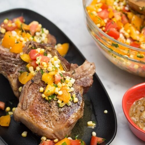 Platter of Sous Vide Double Cut Pork Chops with Raw Summer Corn & Tomato Salad with gravy served alongside.