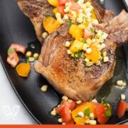 Overhead view of a platter of pork chops with a corn and tomato salad.