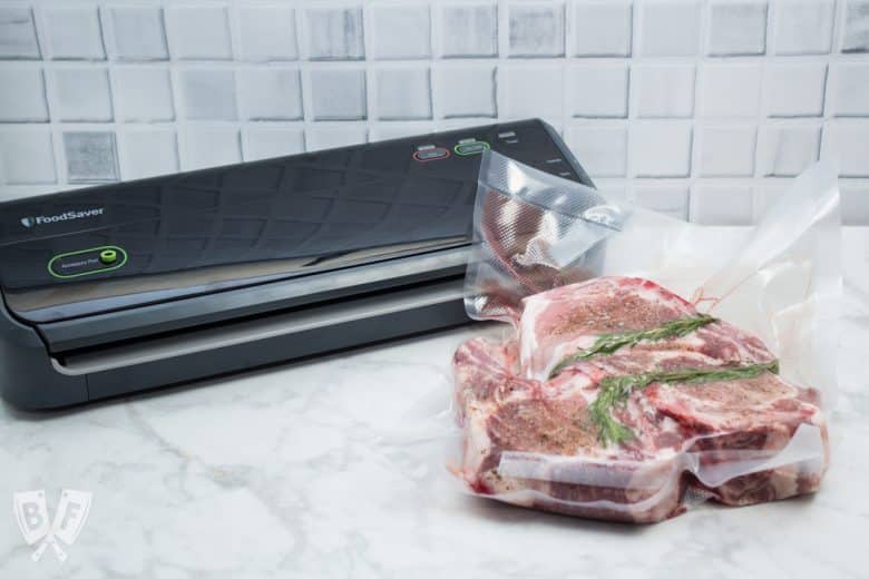 Vacuum seal machine with a bag of sealed double-cut pork chops with rosemary.