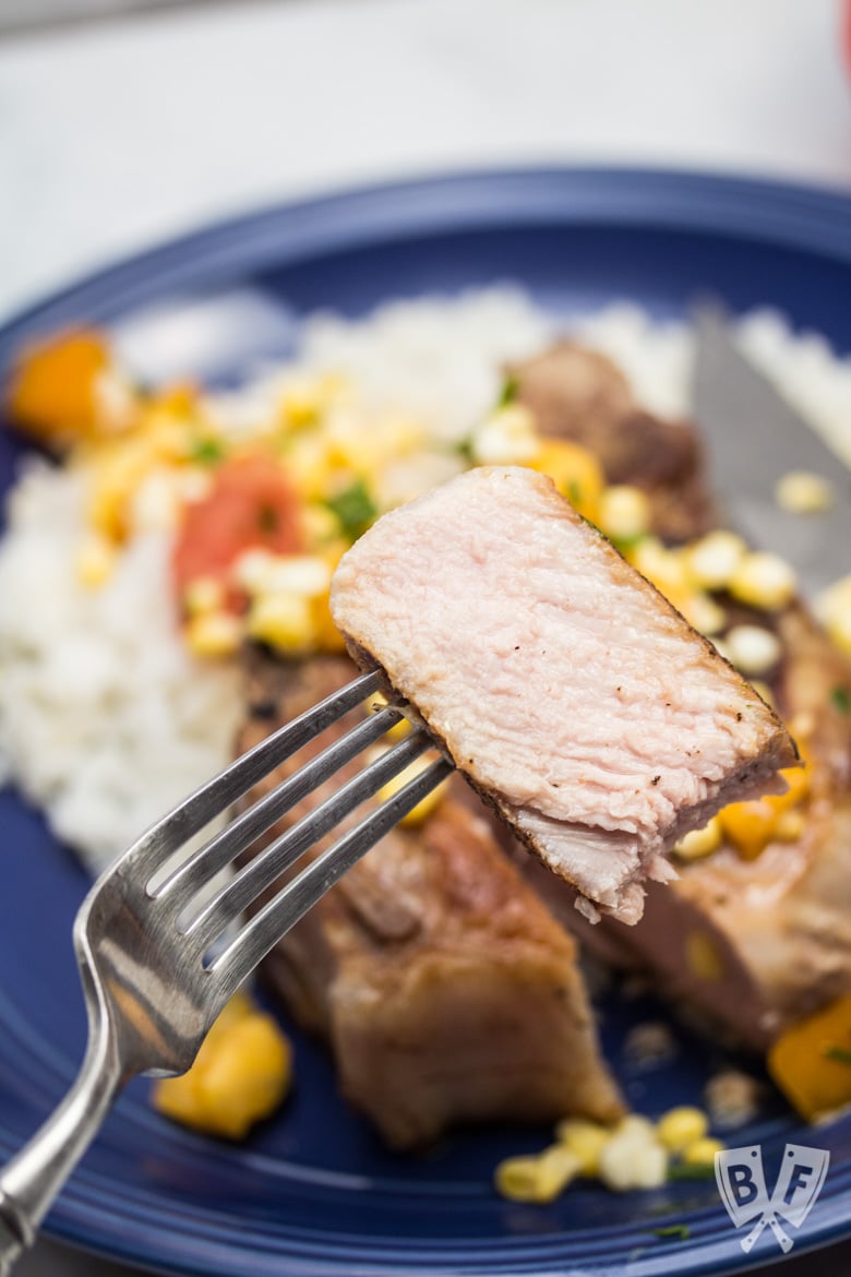 Close up of a cut piece of pork chop served with rice with a corn and tomato salad.