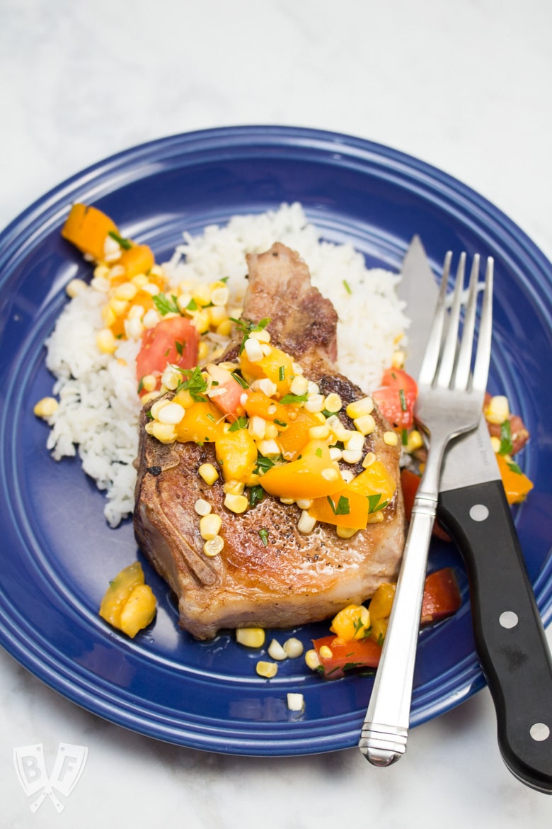 Overhead view of a pork chop over rice with a corn and tomato salad.