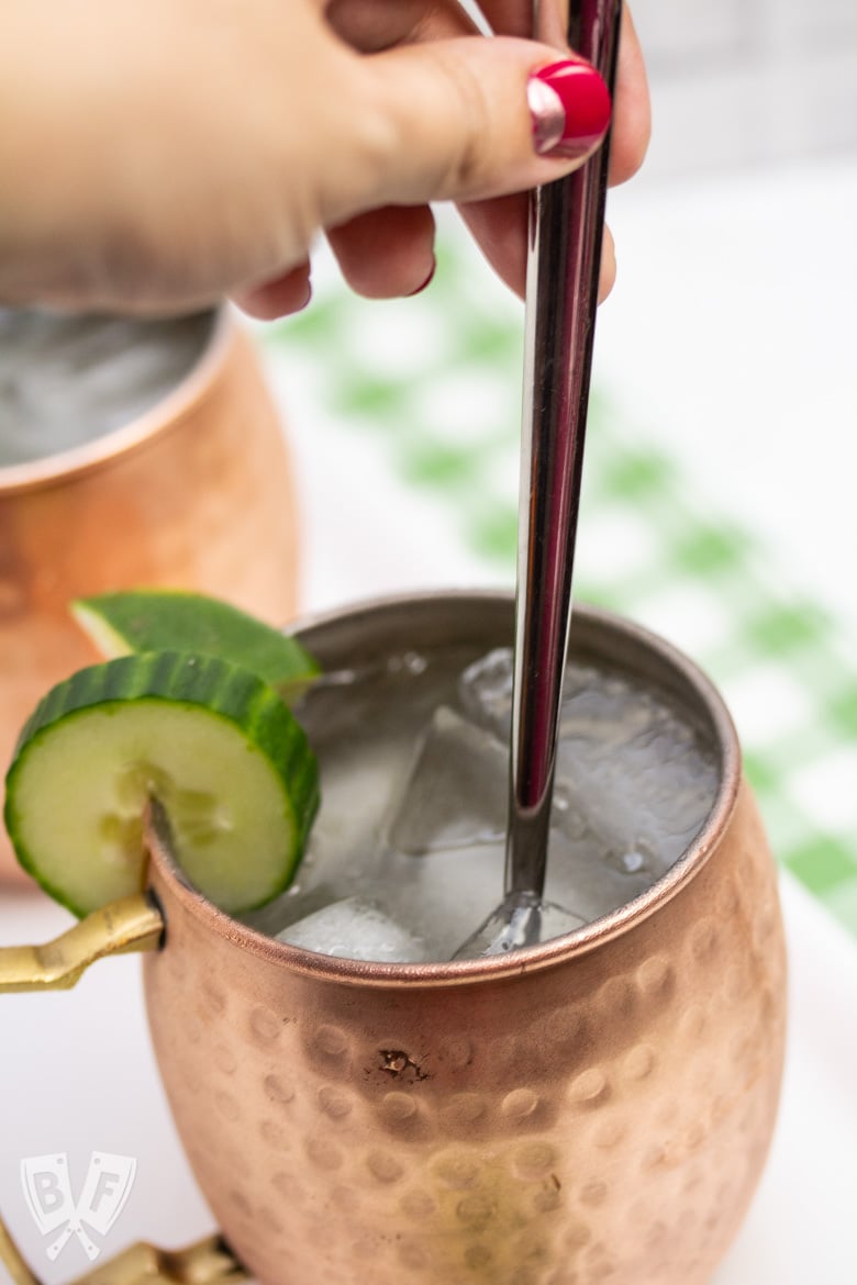 Close up view of stirring a Cucumber Moscow Mule cocktail with a spoon.