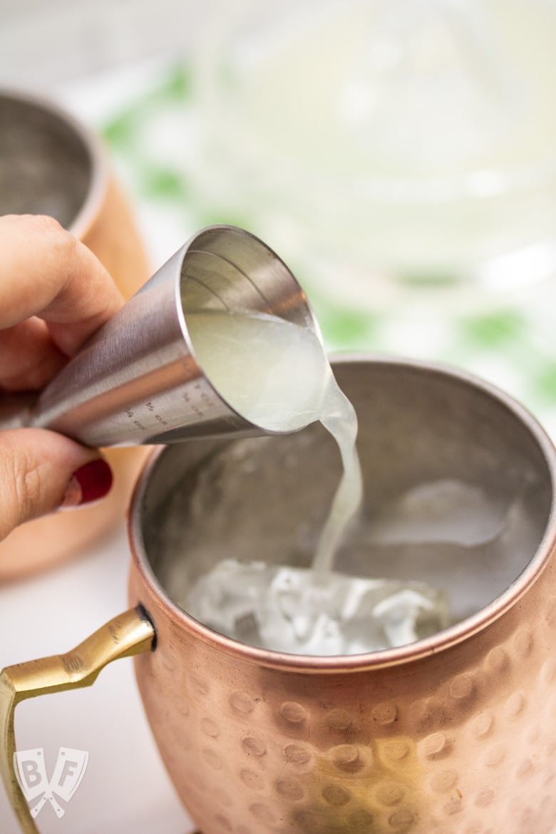 Close up of pouring lime juice into a copper mug for a Cucumber Moscow Mule cocktail.