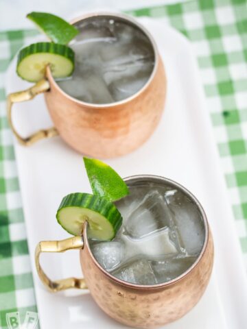 Overhead view of 2 copper mugs filled with a Cucumber Moscow Mule cocktails with ingredients alongside.