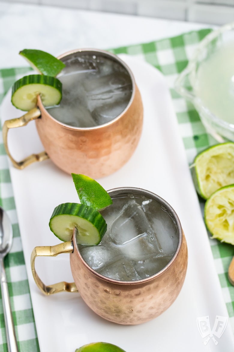 Overhead view of 2 copper mugs filled with a Cucumber Moscow Mule cocktails with ingredients alongside.