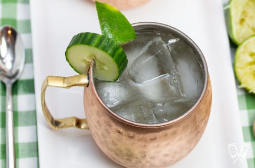 Overhead view of a copper mug filled with a Cucumber Moscow Mule cocktail with ingredients alongside.