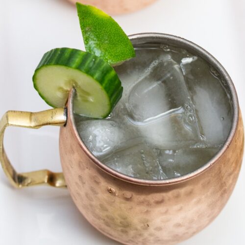 Overhead view of a copper mug filled with a Cucumber Moscow Mule cocktail with ingredients alongside.