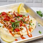 ¾ view of a sheet pan with Falafel-Spiced Chickpea Flatbread on top surrounded by garnishes.