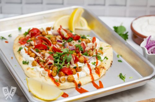 3/4 view of a sheet pan with Falafel-Spiced Chickpea Flatbread on top surrounded by garnishes.