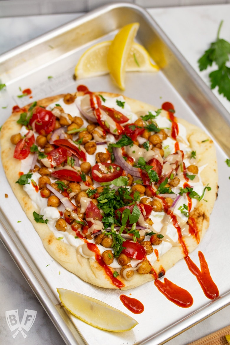 Overhead view of a sheet pan with Falafel-Spiced Chickpea Flatbread on top surrounded by garnishes.