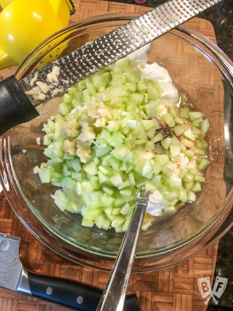 Overhead view of a bowl of yogurt and chopped cucumbers for tzatziki.