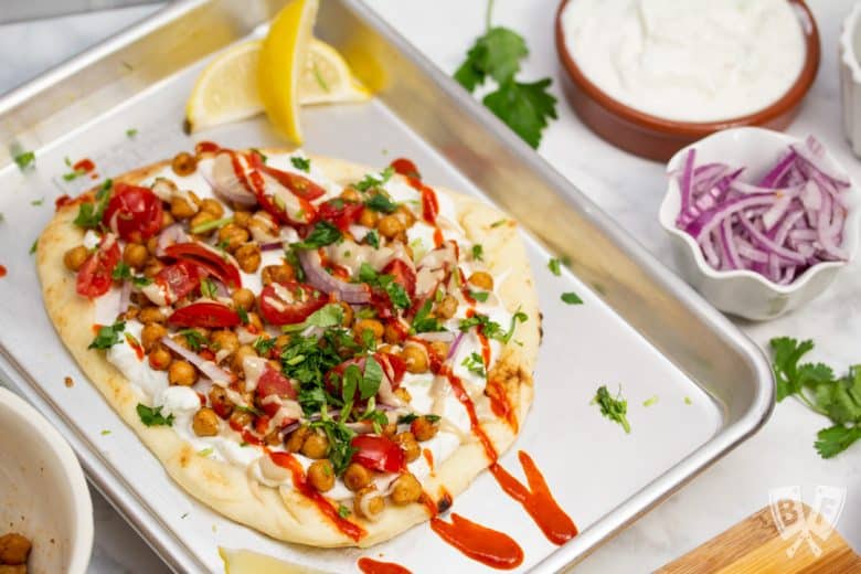 Overhead view of a sheet pan with Falafel-Spiced Chickpea Flatbread on top surrounded by garnishes.