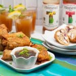 ¾ view of a platter of General Tsao’s Chicken Egg Rolls with a bowl of dipping sauce and glasses and bottles of iced tea.