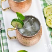 Overhead view of 2 copper mugs filled with Cucumber Moscow Mule cocktails with ingredients alongside.