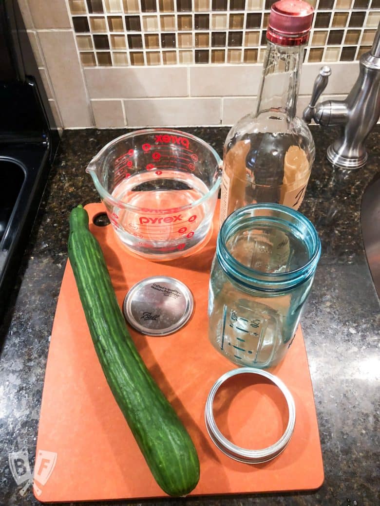 Overhead view of ingredients for homemade cucumber-infused vodka on a cutting board.