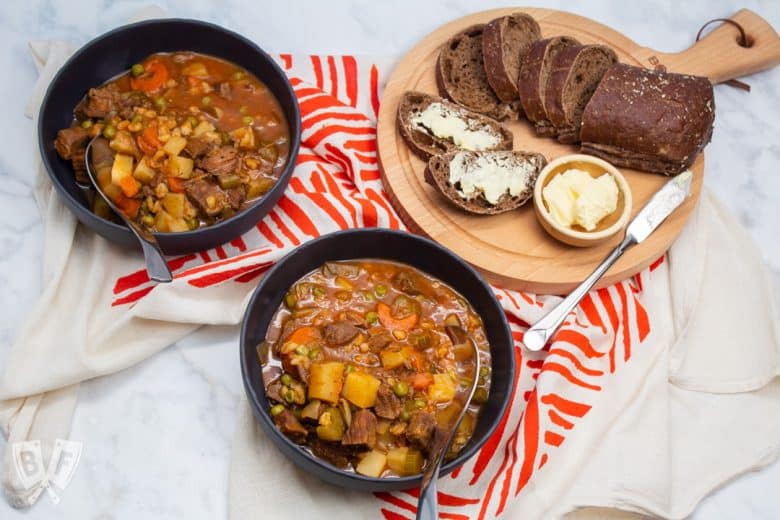 Overhead view of 2 bowls of beef stew with bread and butter.