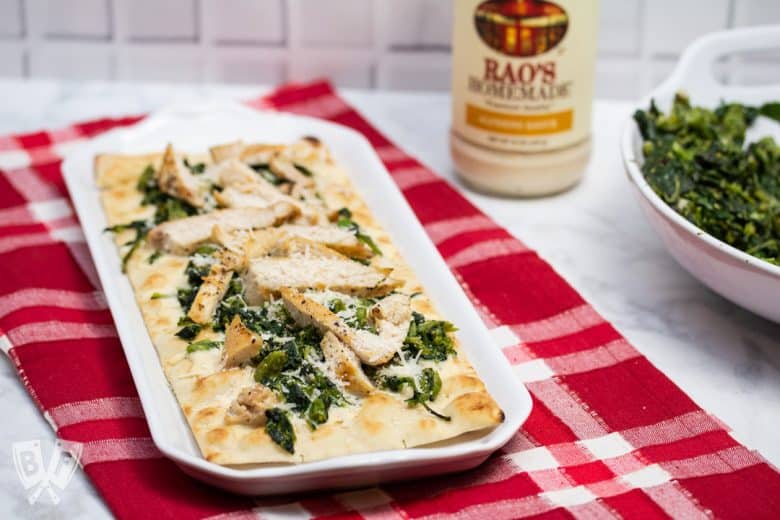 Platter of chicken and broccoli rabe pizza with a jar of alfredo sauce and bowl of broccoli rabe in the background.