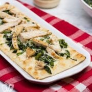Platter of chicken and broccoli rabe pizza with a jar of alfredo sauce and bowl of broccoli rabe in the background.