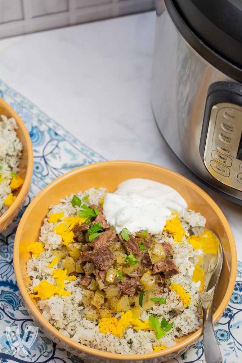 Overhead view of 2 bowls of Instant Pot Persian Beef and Celery Stew (Khoreshe Karafs) with mast-o-khiar over dill rice next to an Instant Pot.