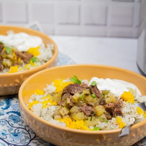 ¾ view of 2 bowls of Instant Pot Persian Beef and Celery Stew (Khoreshe Karafs) with mast-o-khiar over dill rice next to an Instant Pot.