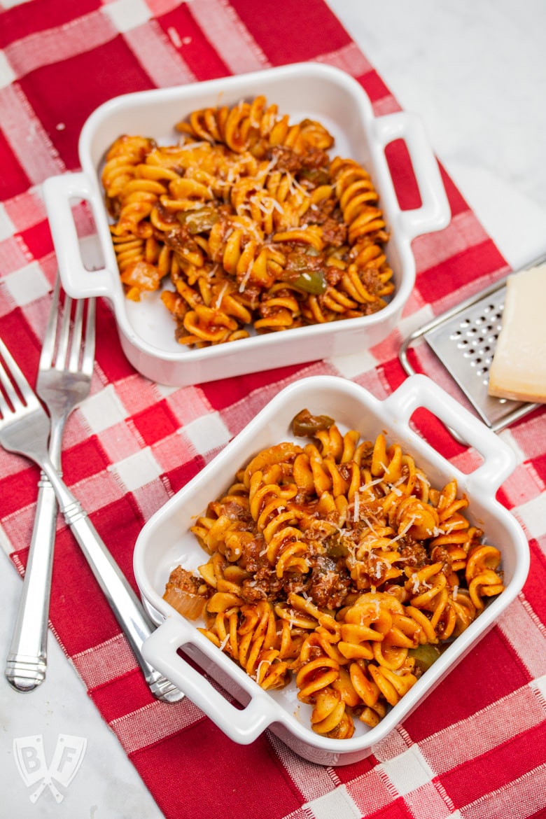 Overhead view of dishes of Instant Pot Tomato Beef Pasta with serving dishes with Parmesan cheese in the background.