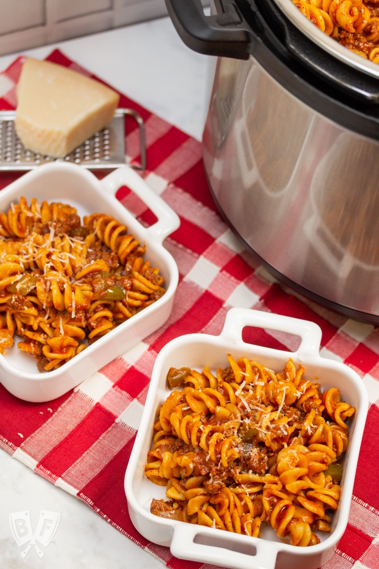 Overhead view of dishes of Instant Pot Tomato Beef Pasta with serving dishes with Parmesan cheese in the background.